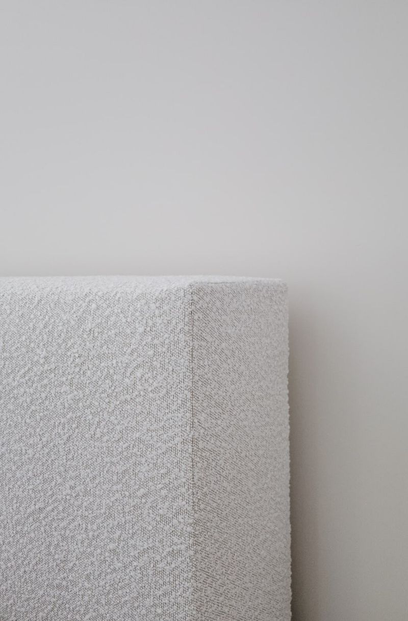 A cream boucle upholstered headboard in a Clive bedroom, set against a soft warm white wall.