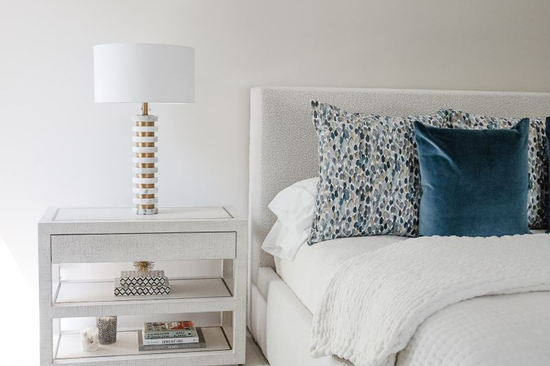 A bedroom in Clive with a stacked marble and brass lamp on a white grasscloth nightstand.