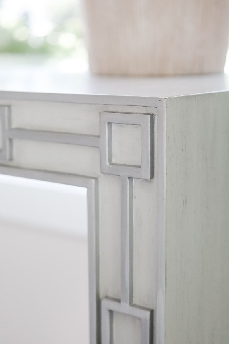 A pale gray painted console table in Clive with a Greek key fretwork detail carved into its corner.