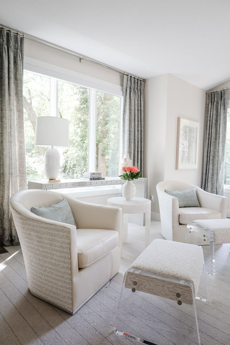 A cream living room in Clive with four ivory swivel chairs and gray pleated drapes at the windows.