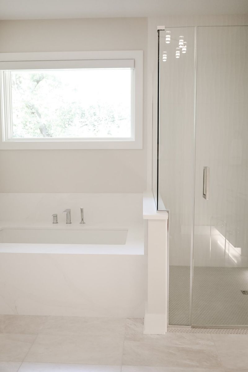 A white primary bath in Clive with a marble-look tub deck beside a glass shower on penny tile floor.