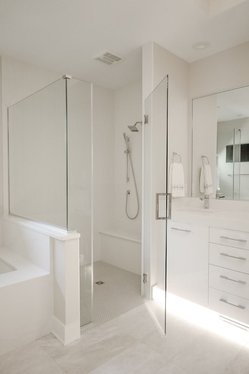 An all white primary bath in Clive with a glass walk in shower over a penny tile floor.