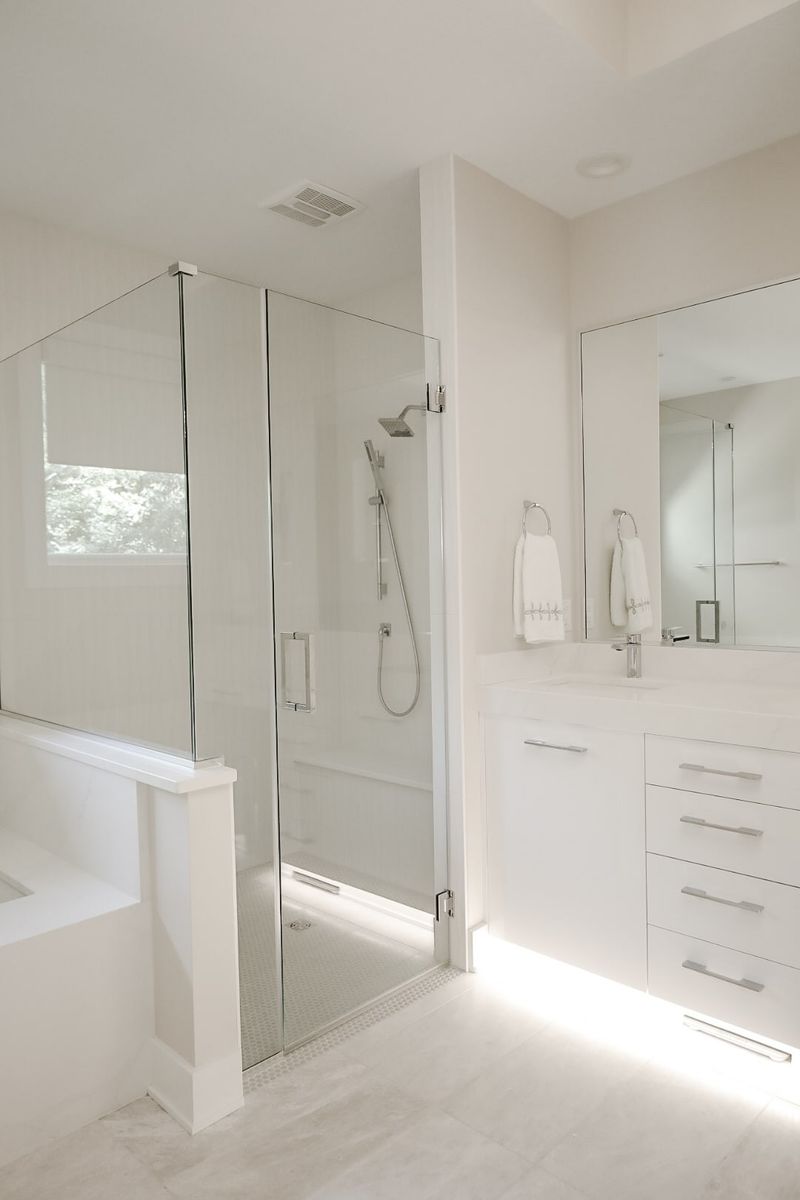 An all white primary bath in Clive with a glass walk in shower over penny tile flooring.