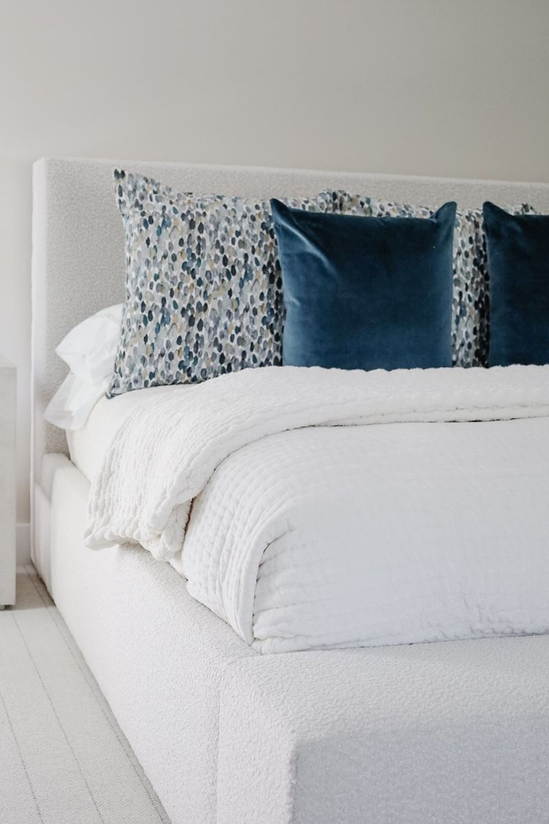 A primary bedroom in Clive with navy velvet pillows against a cream boucle upholstered headboard.