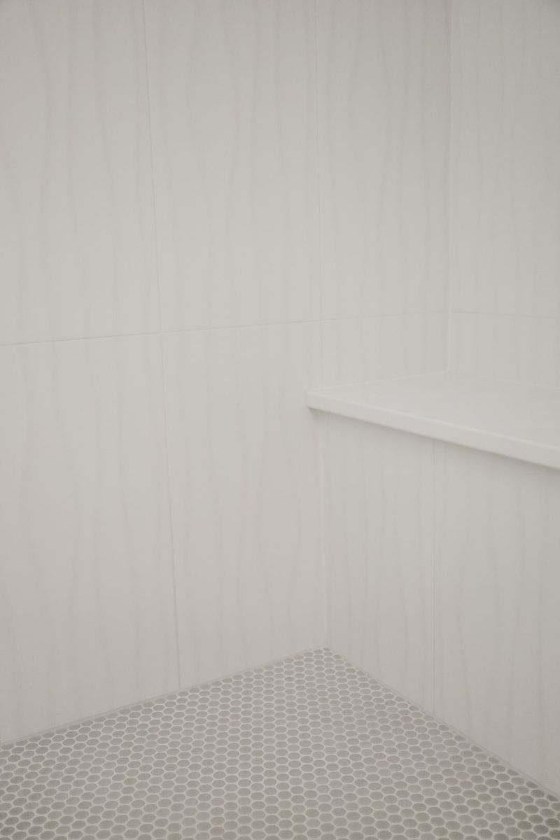 A white shower in Clive with a built in bench above a gray penny tile floor.