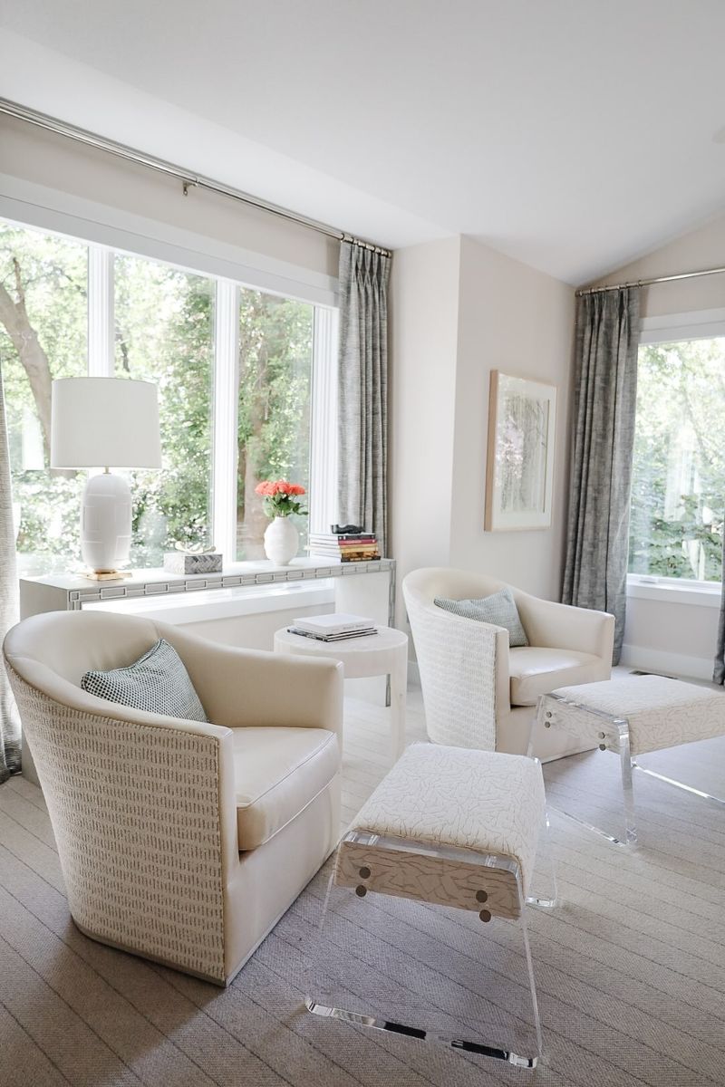 A cream sitting room in Clive with two textured barrel chairs and lucite benches on a pale wool rug.