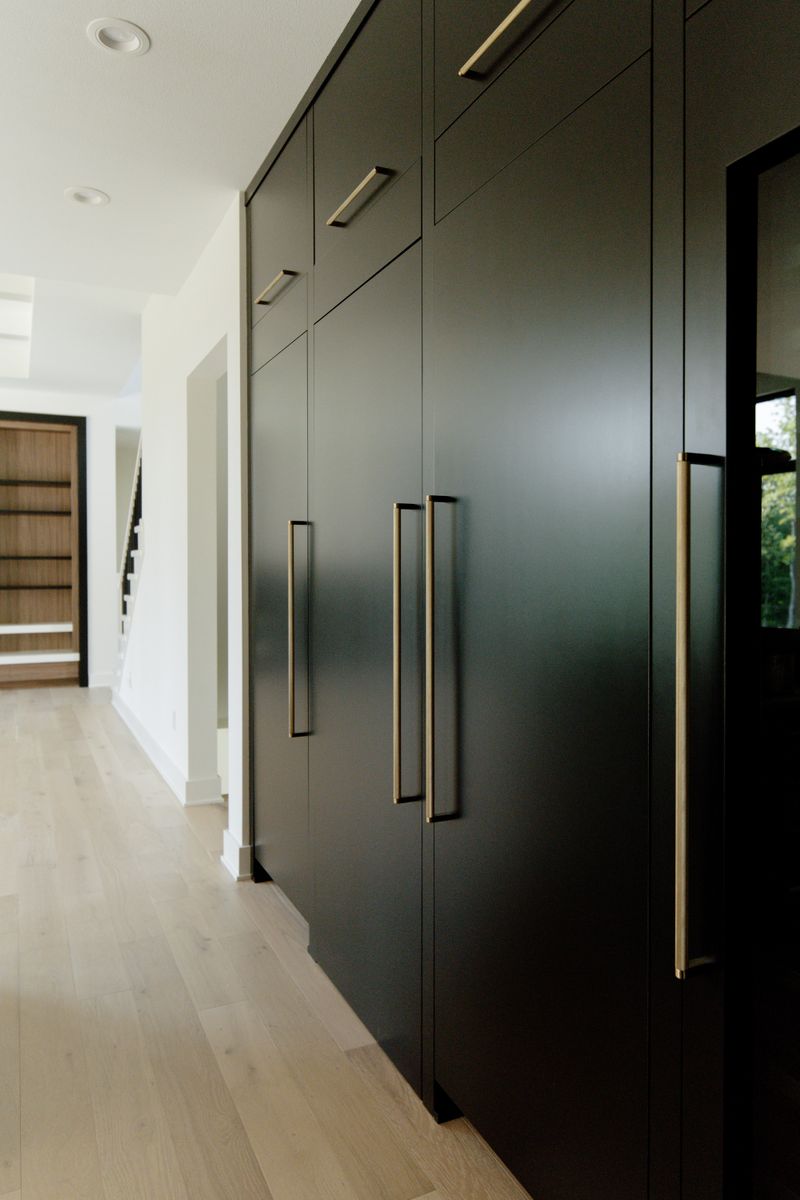A kitchen in Waukee with floor to ceiling black cabinets and long brass pulls above pale oak floors.