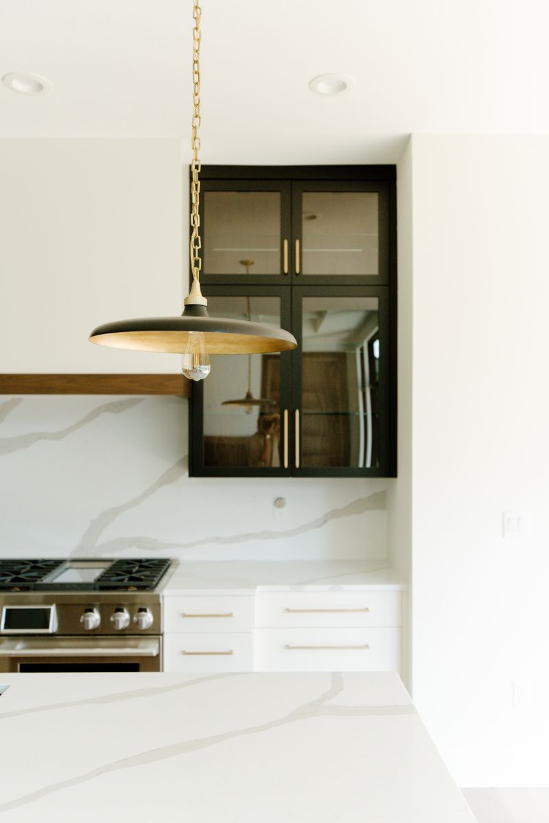A white kitchen in Waukee with a black glass front cabinet and a brass pendant over the marble backsplash.
