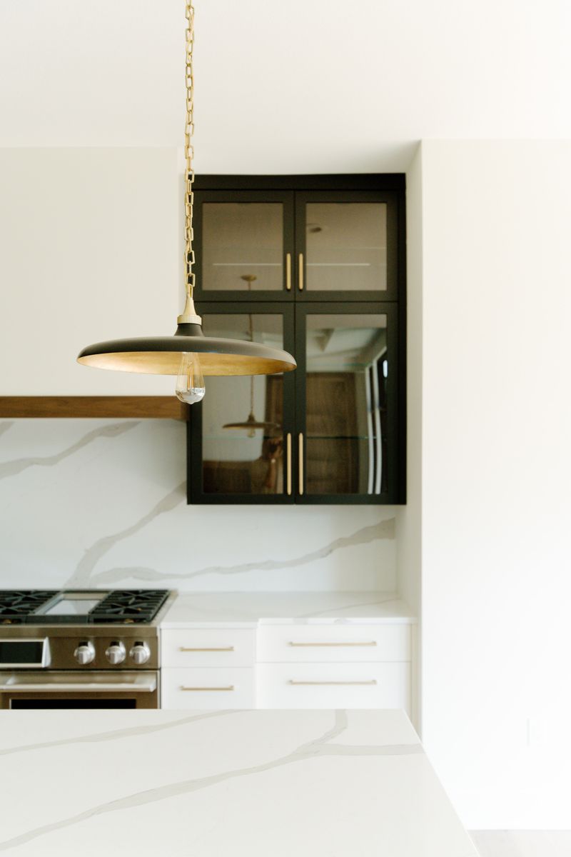 A white kitchen in Waukee with a black glass-front cabinet above the marble backsplash and brass pulls.