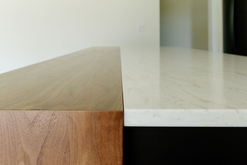 A kitchen island in Waukee where a white veined quartz counter meets a walnut waterfall edge.