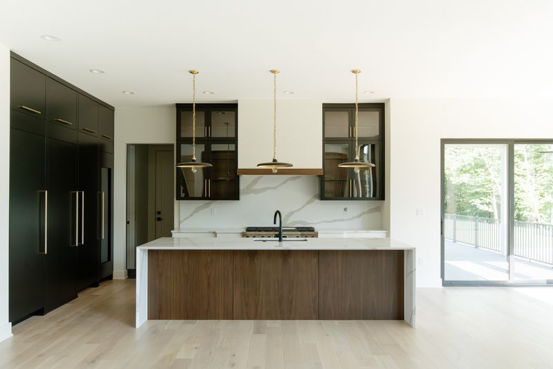 A kitchen in Waukee with a walnut island under a waterfall marble countertop and brass pendant lights.