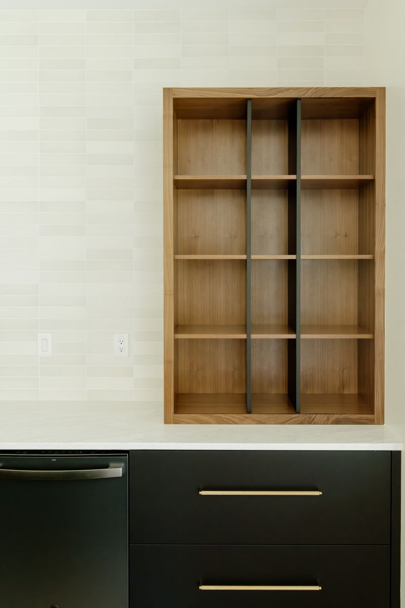 A kitchen in Waukee with open white oak shelving set into a cream tile backsplash above dark green cabinets.