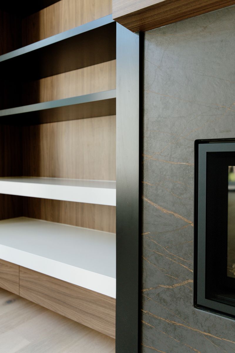 A living room in Waukee with a gray veined stone fireplace surround next to walnut built-in shelving.