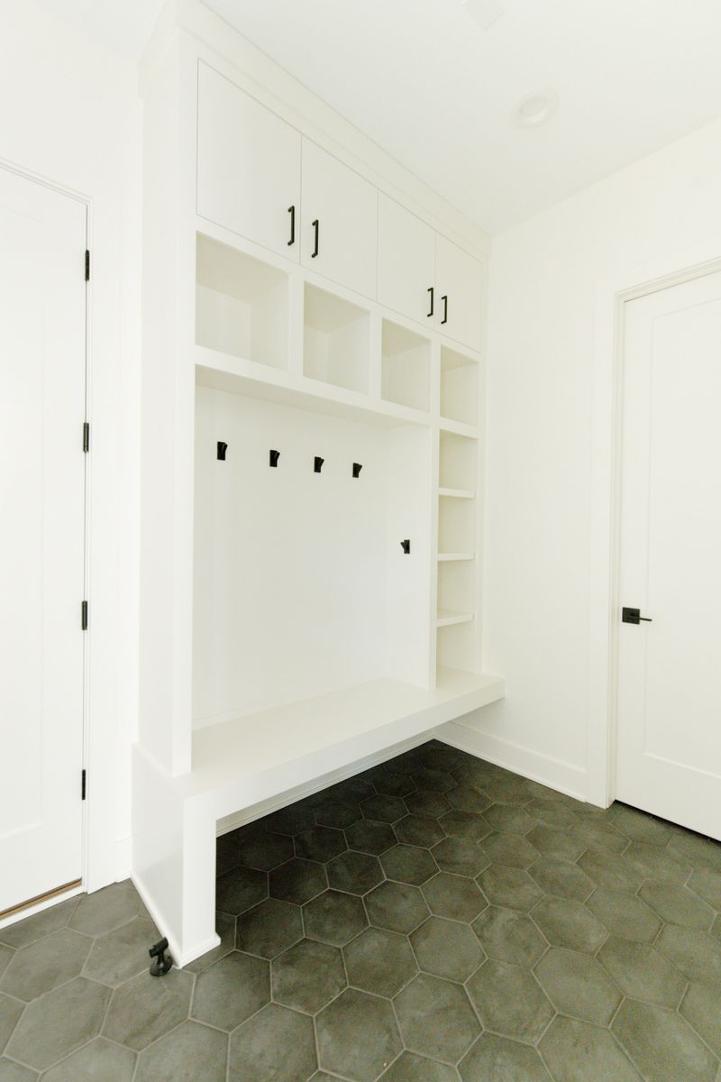 A white built-in mudroom bench in Waukee sitting over gray hexagon tile floors.