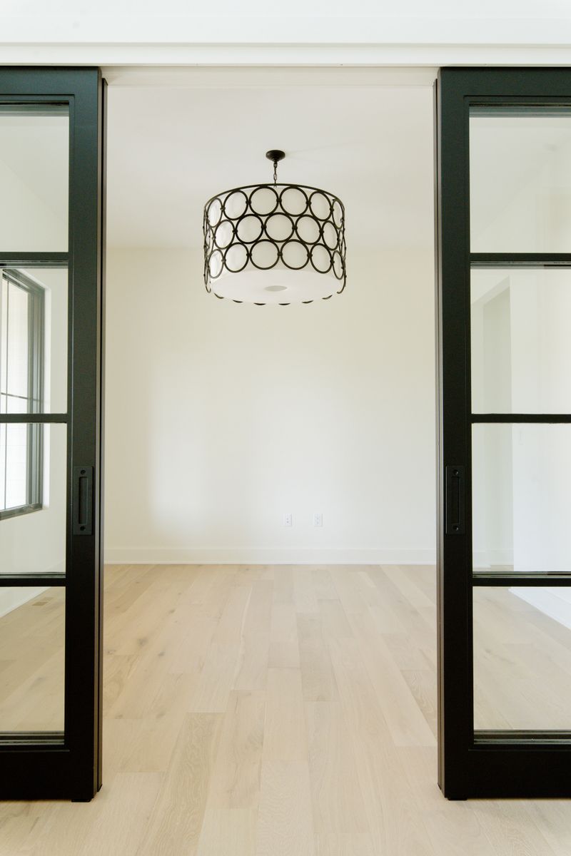 A home office in Waukee behind black steel and glass pocket doors, with white oak floors and a bronze ring pendant.
