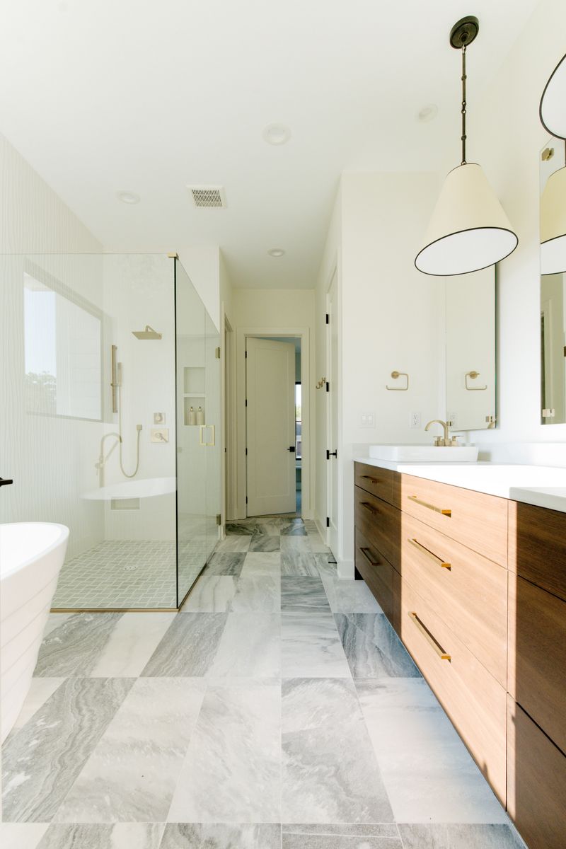 A primary bath in Waukee with a walnut vanity and brass pulls set against gray marble floor tile.