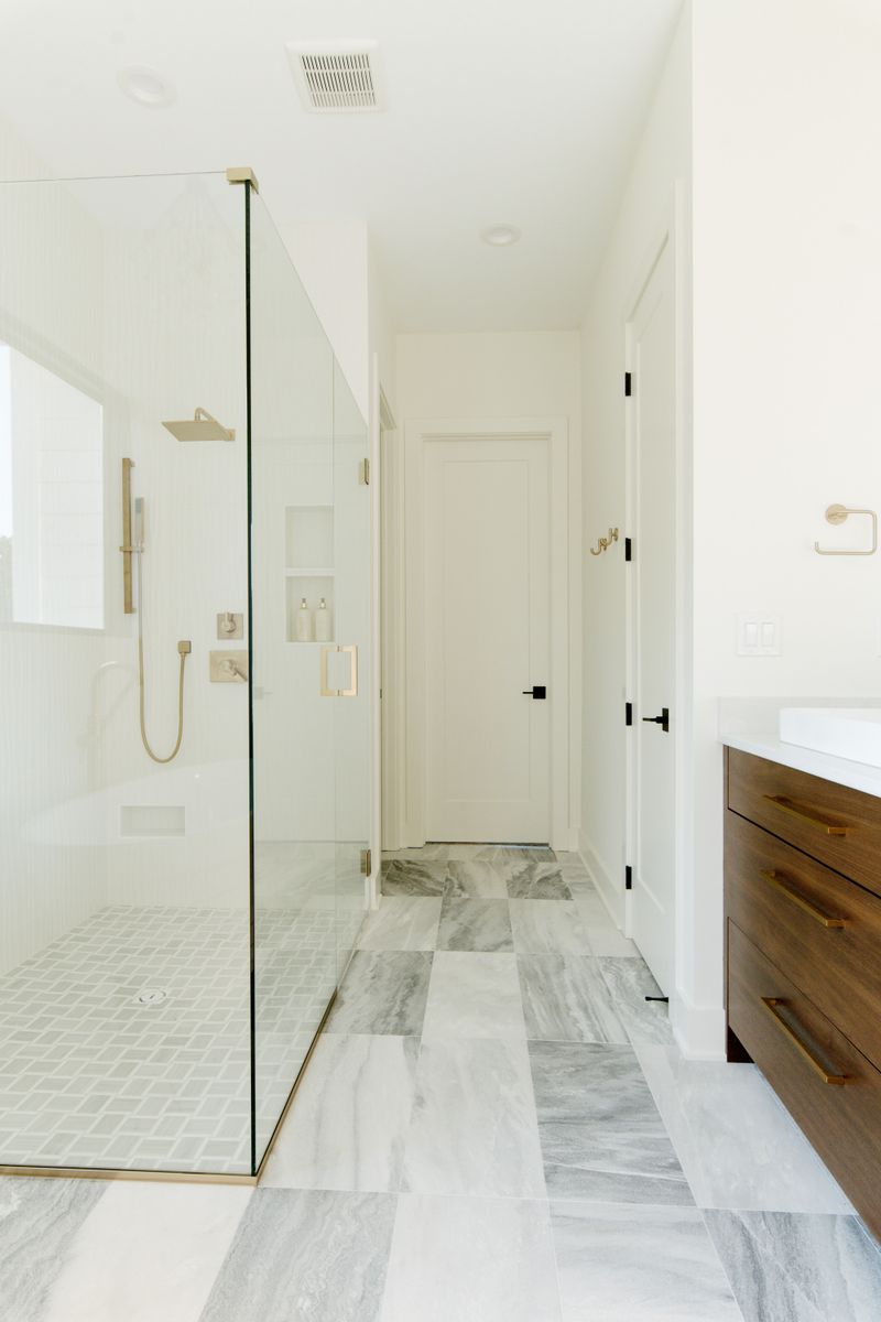 A primary bath in Waukee with gray marbled floor tile running up to a walnut floating vanity.