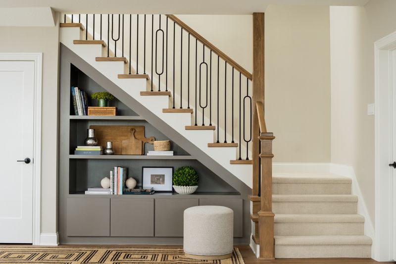 A staircase entry in Van Meter with gray built-in shelves tucked under the stairs and black iron balusters.