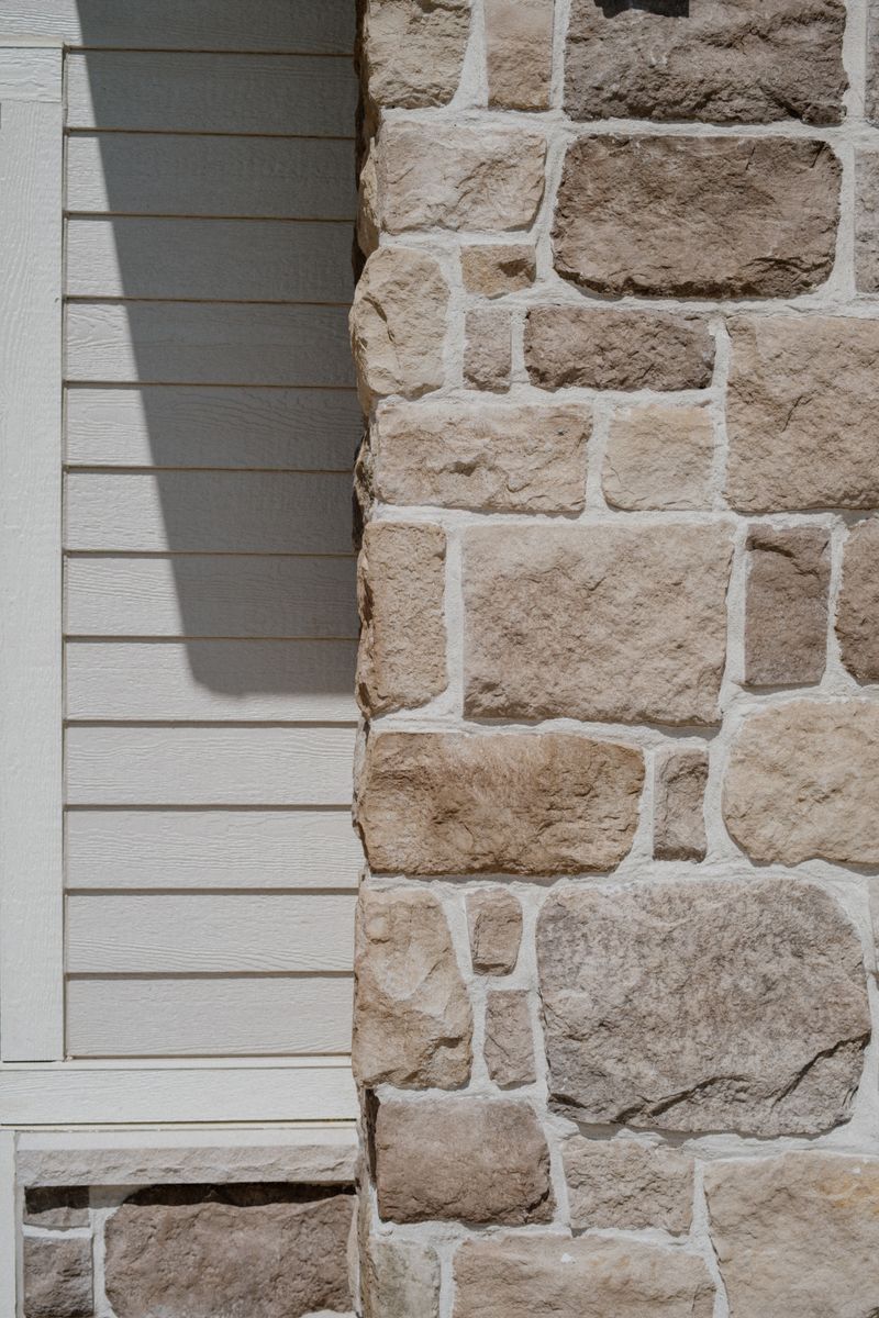 A Van Meter home exterior where cream lap siding meets a limestone stone column with wide white mortar joints.