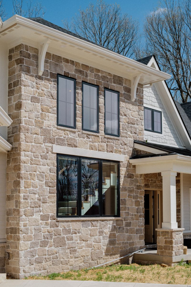 A limestone home exterior in Van Meter with black windows set against white shingle siding.