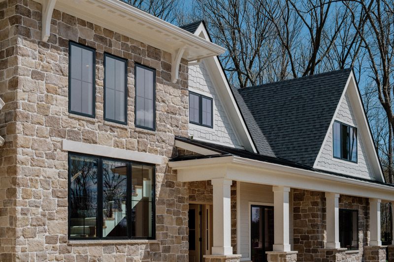 A limestone home exterior in Van Meter with black windows set against a white shingled gable.