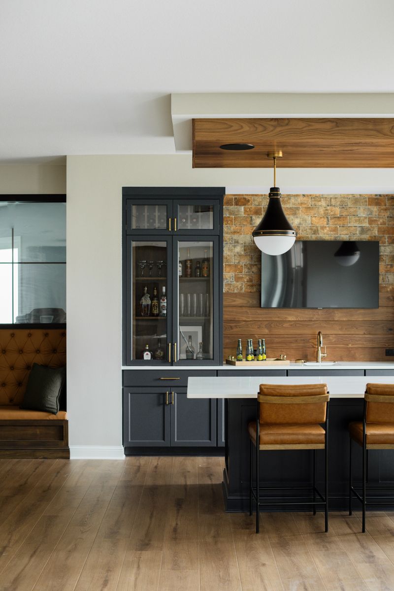 A home bar in Van Meter with navy cabinets and a walnut plank wall above a brick backsplash.