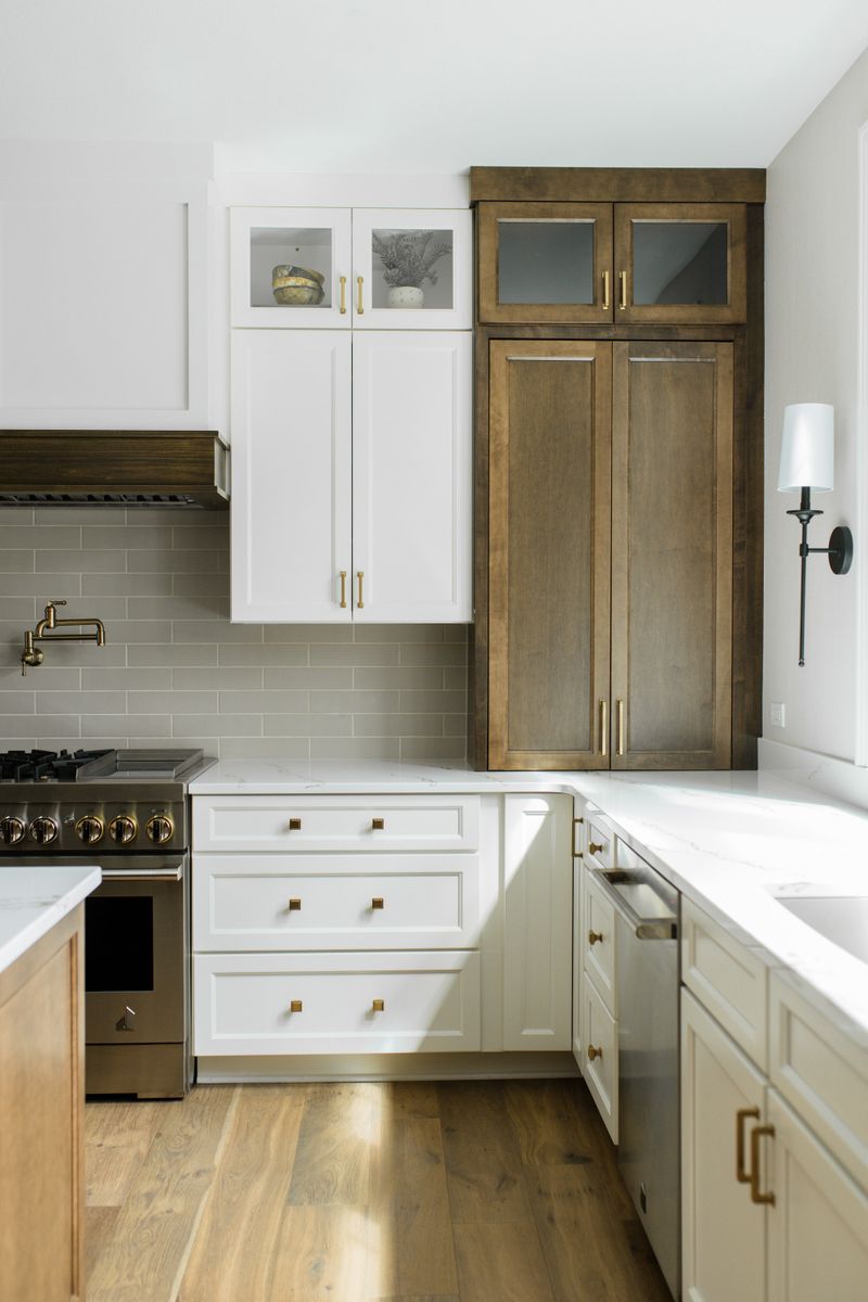 A white kitchen in Van Meter with a stained wood pantry cabinet beside a brass pot filler over the range.