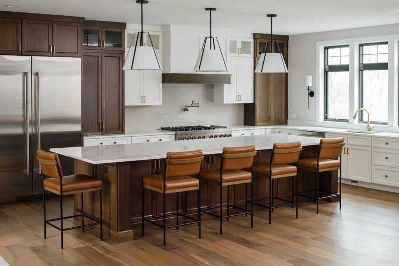 A white kitchen in Van Meter with tan leather stools at a dark wood island under a quartz counter.
