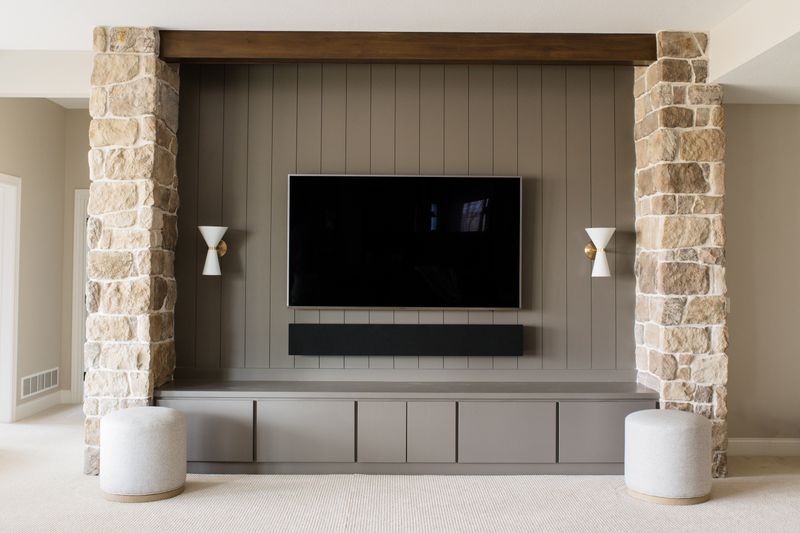 A living room in Van Meter with a greige vertical shiplap media wall built beside a limestone column.