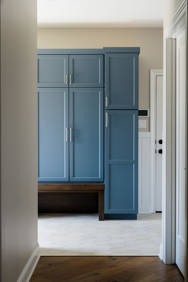 A mudroom in Van Meter with blue cabinets over a dark wood bench, set on white hexagon tile.