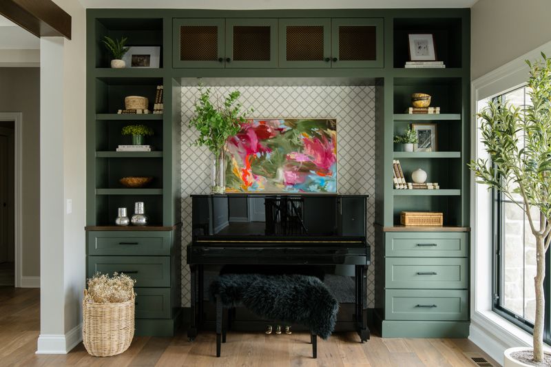 A music room in Van Meter with green built-in shelving around a black upright piano.