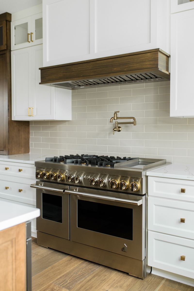 A white kitchen in Van Meter with a stained wood hood over a double range, above greige subway tile.