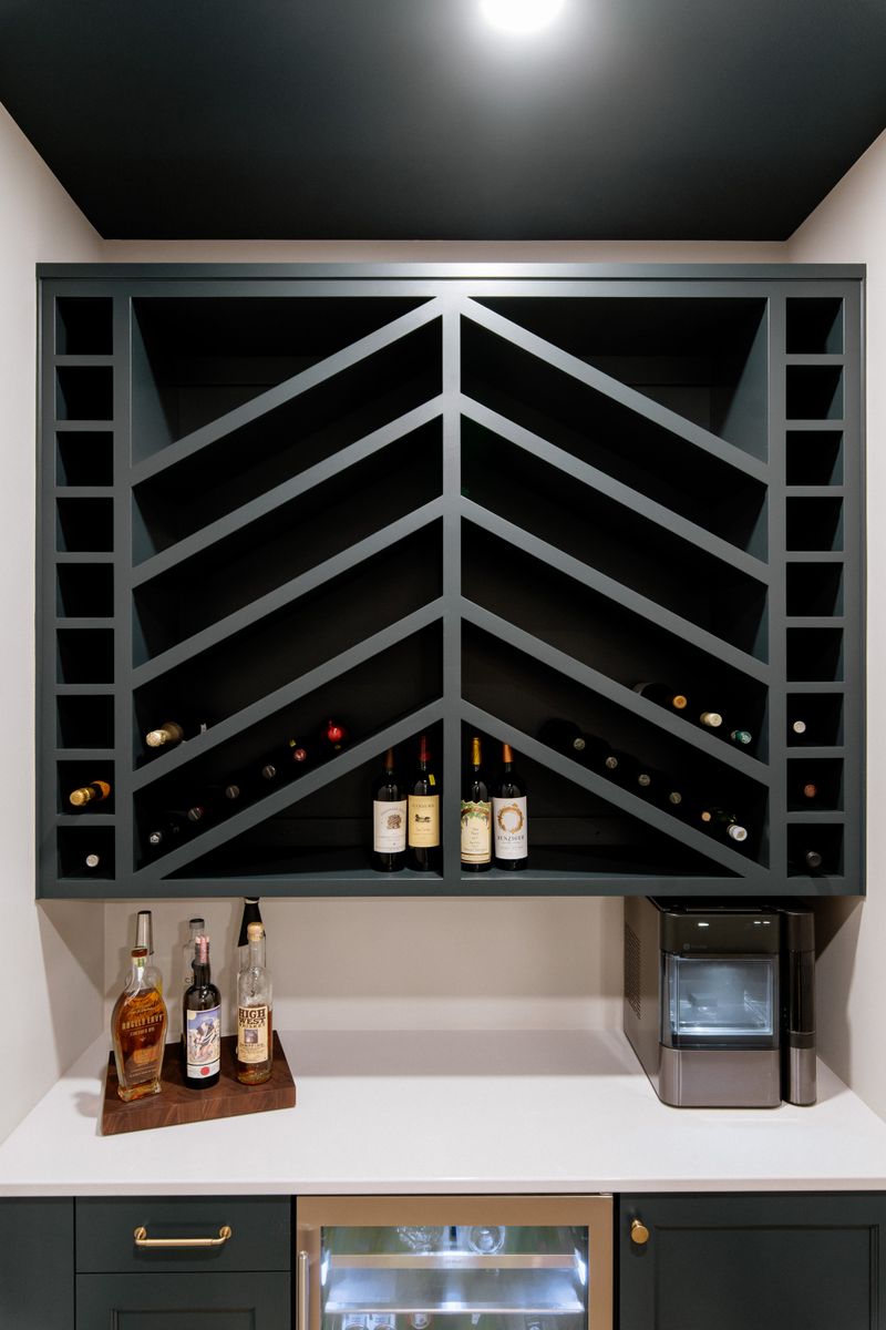 A home bar in Urbandale with a dark green chevron wine rack built into the wall above the counter.