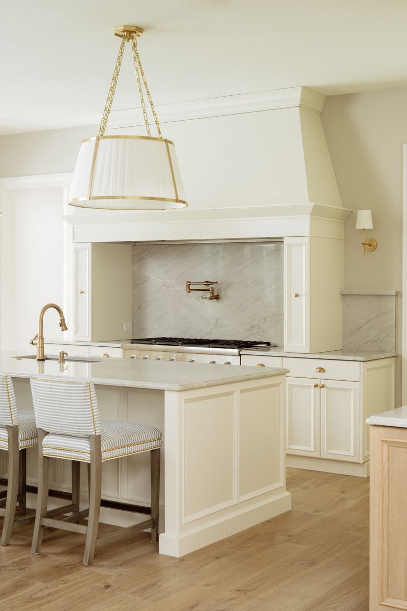 A cream kitchen in Urbandale with a plaster hood over a marble slab backsplash and a brass pot filler.