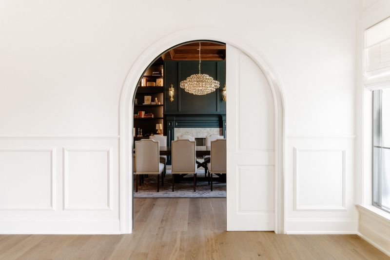 A dark green dining room in Urbandale with a crystal chandelier over the table, seen through an arched doorway.