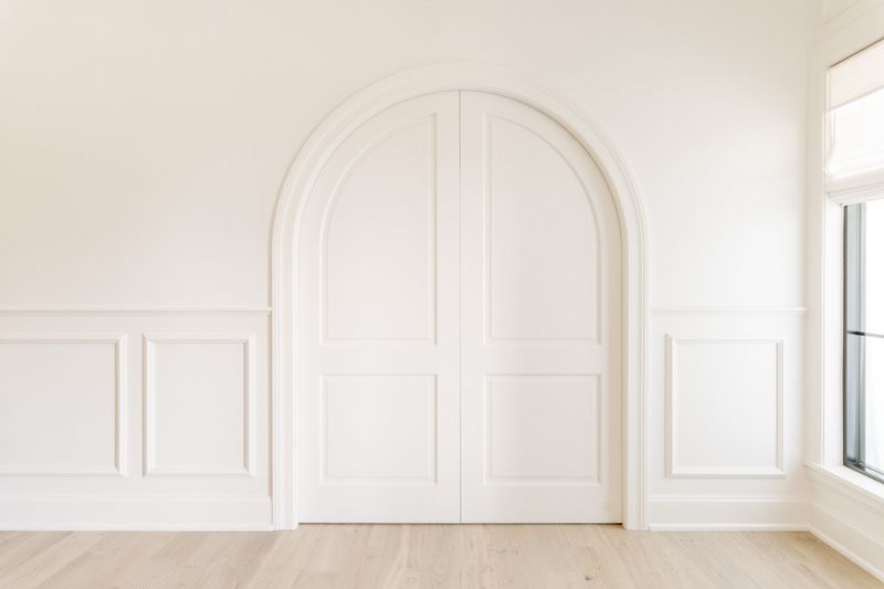 A white entry in Urbandale with an arched double door beside picture frame wall molding and pale oak floors.