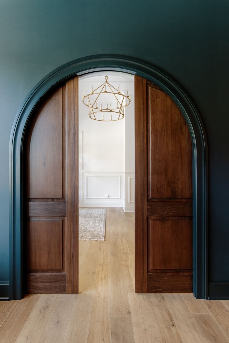 A dark green arched pocket door in Urbandale with stained wood doors opening to a brass ring chandelier.