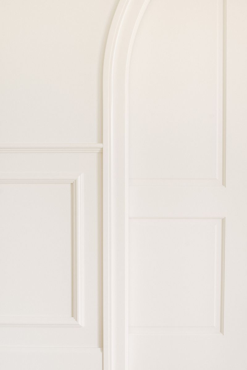 A hallway in Urbandale with creamy white wall paneling meeting a paneled door in the same soft finish.