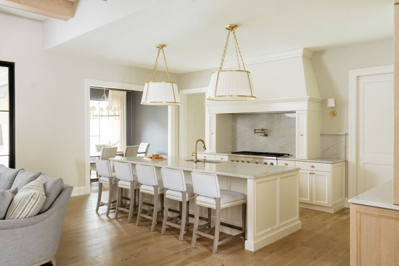 A cream kitchen in Urbandale with brass shade pendants over a white marble island and striped counter stools.