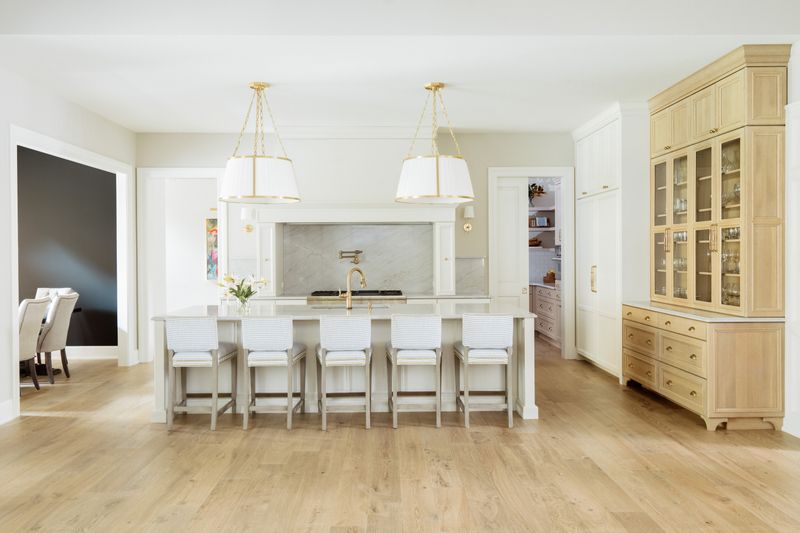 A white kitchen in Urbandale with a marble slab backsplash behind the range and brass fixtures over white oak floors.
