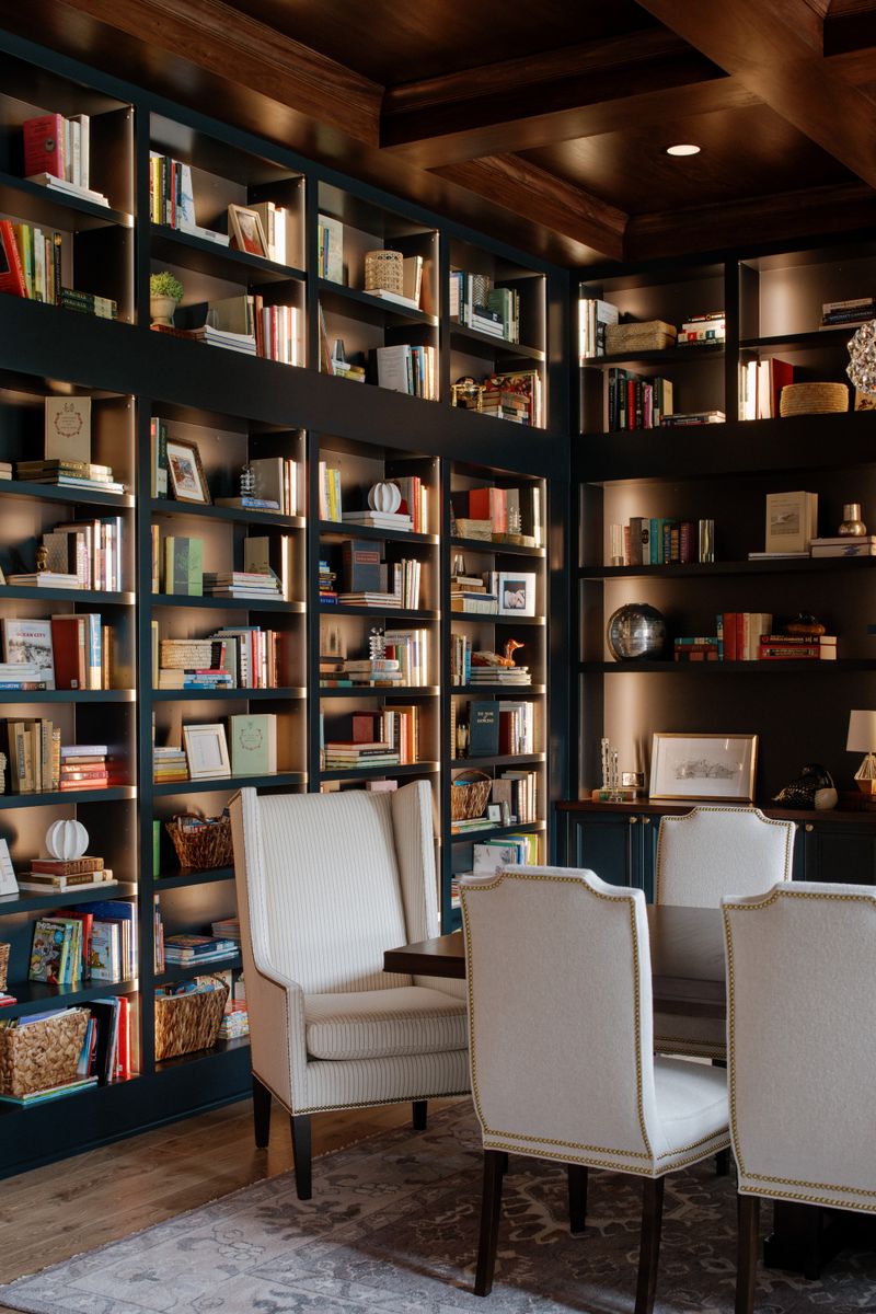 A home library in Urbandale with navy built-in bookshelves and white nailhead chairs around a dark wood table.