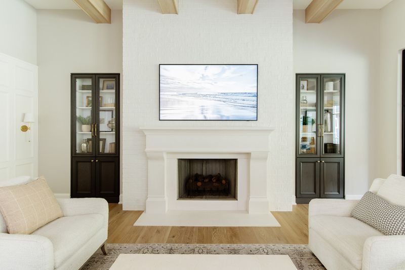 A living room in Urbandale with a dark green glass front cabinet beside a white painted brick fireplace.