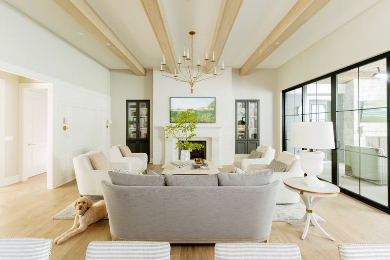 A bright living room in Urbandale with white oak ceiling beams above black steel sliding glass doors.