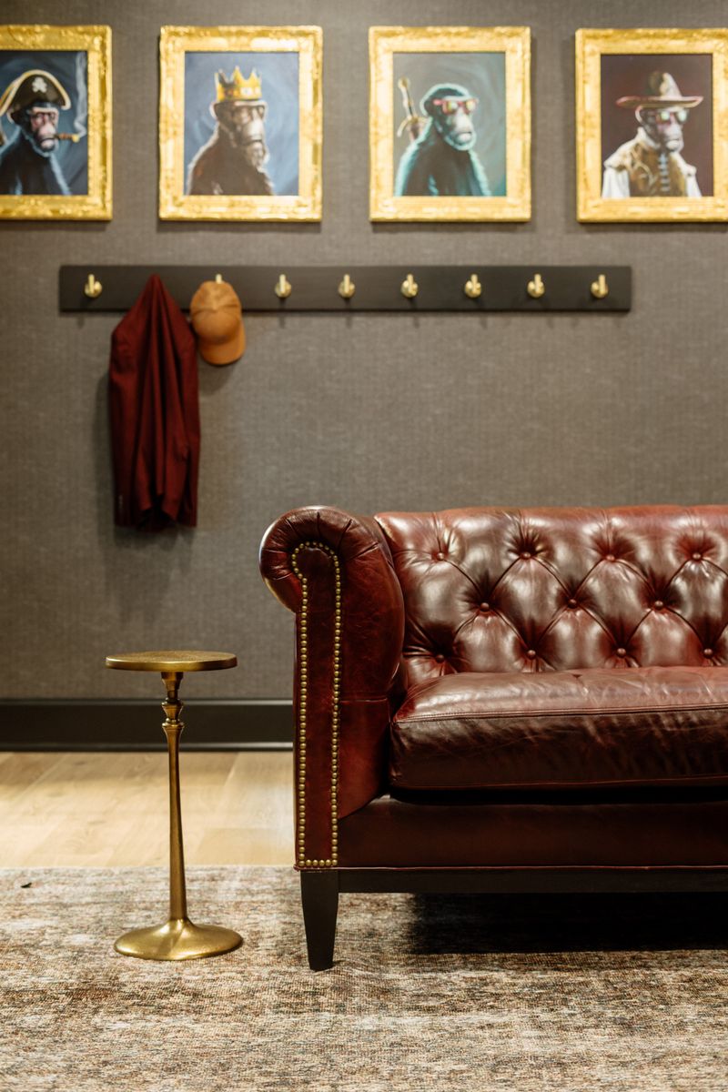 A mudroom in Urbandale with a tufted oxblood leather sofa below a black coat rail with brass hooks.