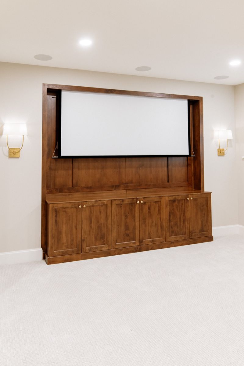 A media room in Urbandale with a stained wood built-in framing the projector screen, brass knobs on the cabinet doors.
