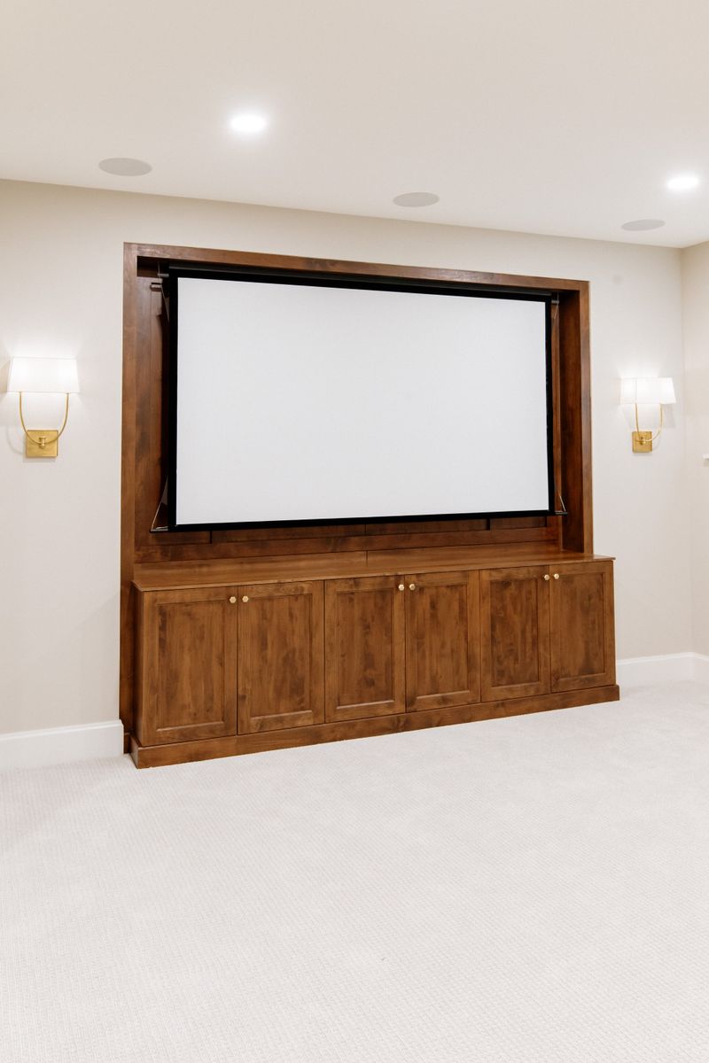 A media room in Urbandale with a stained wood built-in surrounding the projection screen and brass sconces on either side.