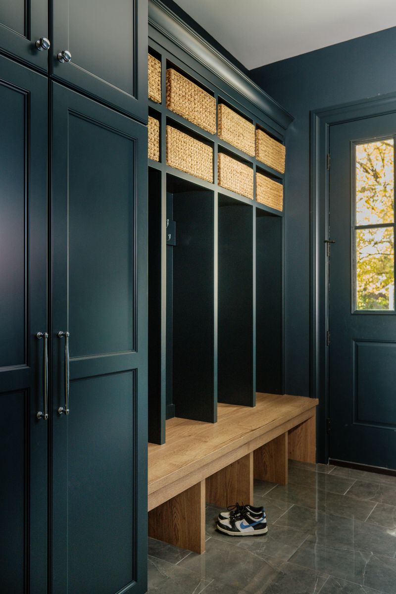 A dark teal mudroom in Urbandale with an oak bench built into the lockers and woven baskets stored above.
