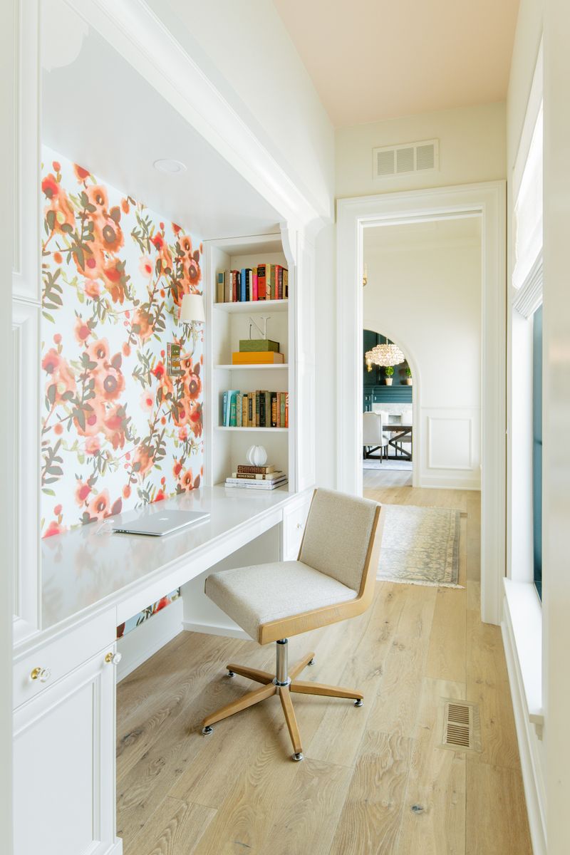 A built-in office nook in Urbandale with coral floral wallpaper above a white desk and pale oak floors.