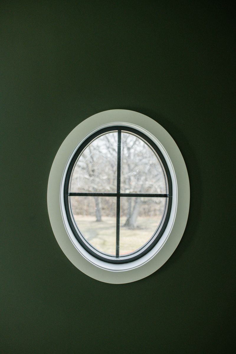 An oval window with black grilles set into a dark green painted wall in a house under construction in Urbandale.