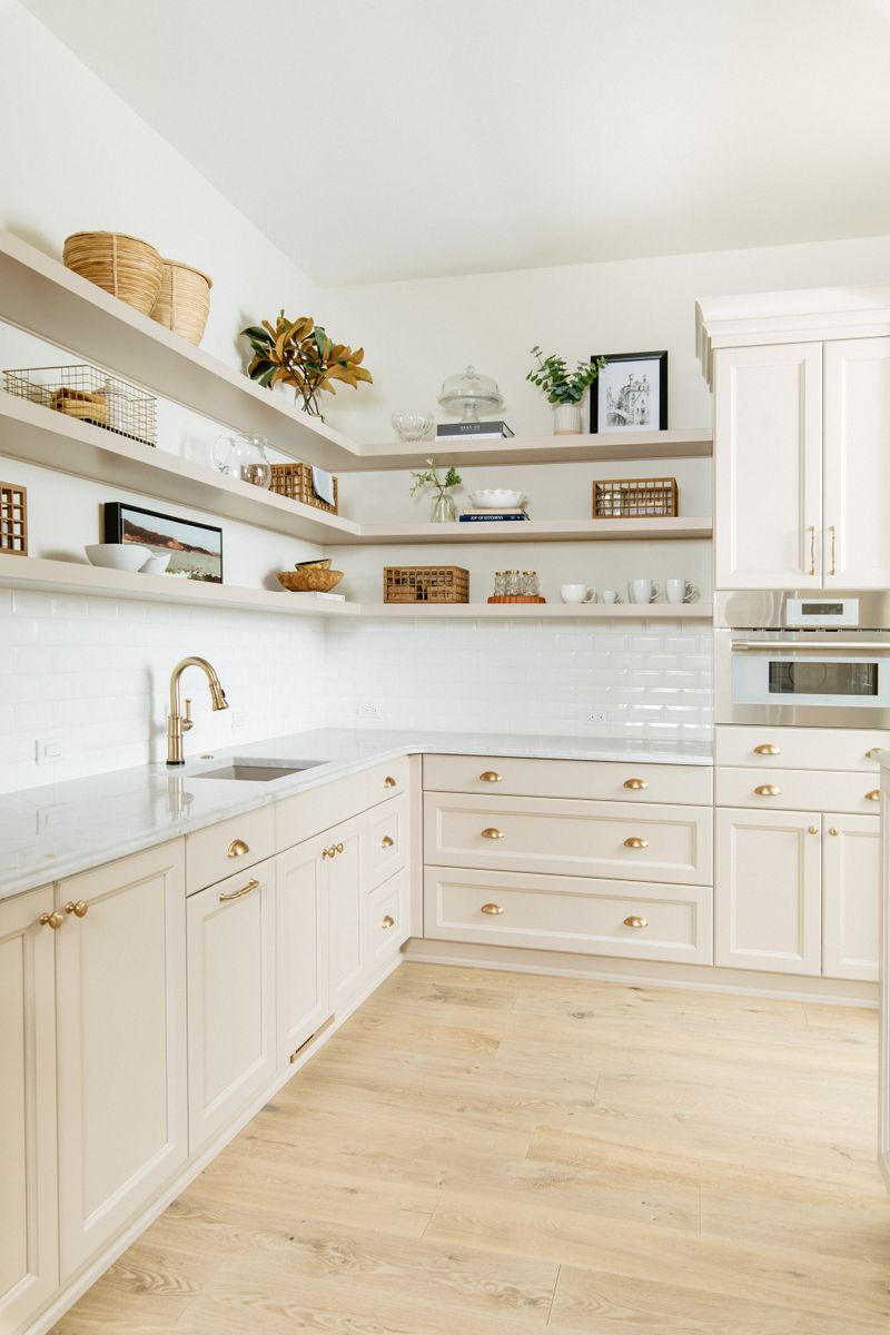 A cream pantry in Urbandale with brass cup pulls on the cabinets and open shelves above white tile.